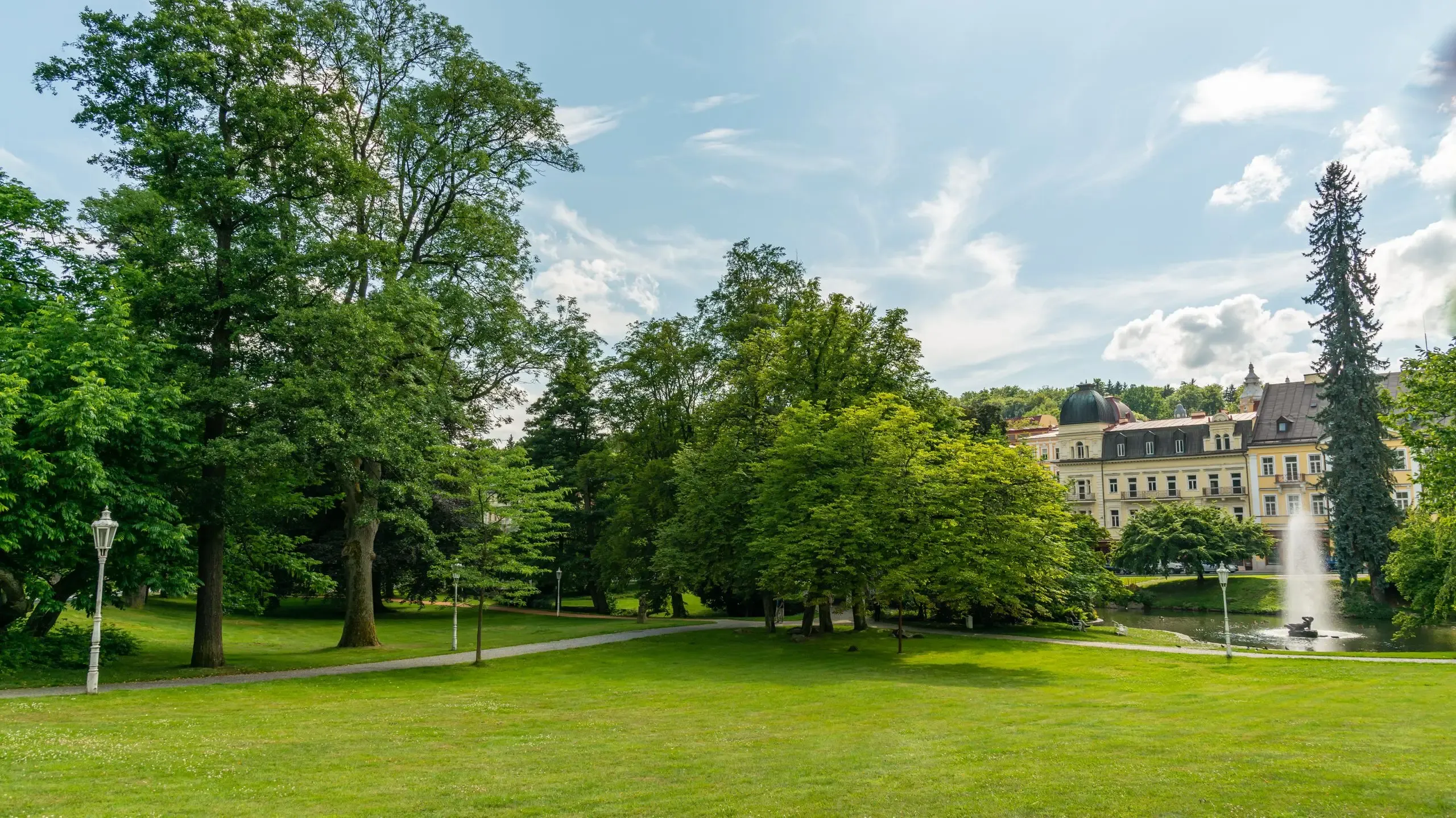 A scenic park featuring a central fountain surrounded by lush green trees and vibrant flowers